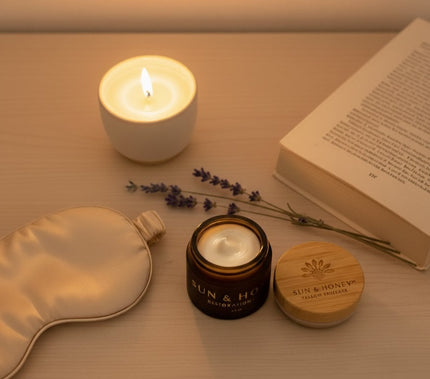 Nightstand flatlay with Sun & Honey tallow balm jar, bamboo lid, silk sleep mask, candle, and open book - evening skincare ritual for mature skin.