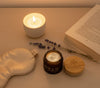 Nightstand flatlay with Sun & Honey tallow balm jar, bamboo lid, silk sleep mask, candle, and open book - evening skincare ritual for mature skin.